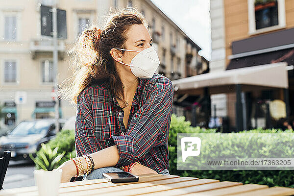 Woman wearing protective face mask while sitting at sidewalk cafe during pandemic