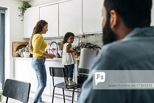 Vater sieht Tochter an  die Mutter in der Küche hilft