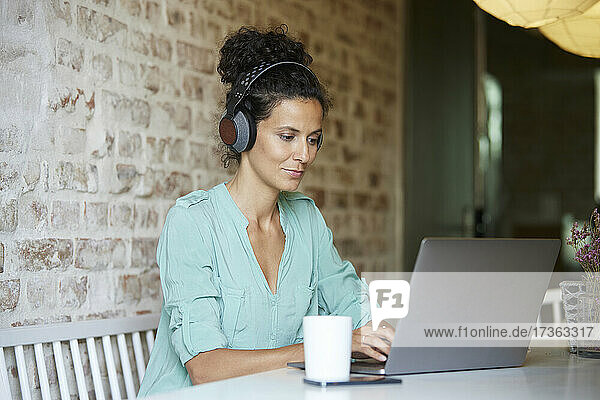 Geschäftsfrau mit drahtlosen Kopfhörern  die einen Laptop am Schreibtisch im Büro benutzt