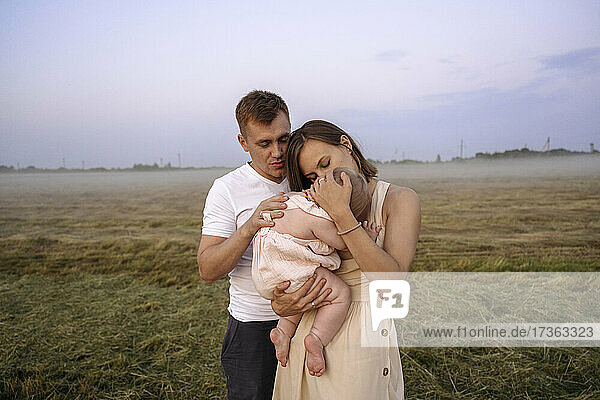 Mutter und Vater umarmen gemeinsam ihre Tochter auf einem Feld bei Sonnenuntergang