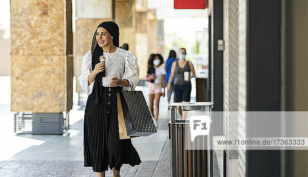 Lächelnde junge Frau  die ein Eis isst  während sie auf dem Fußweg geht