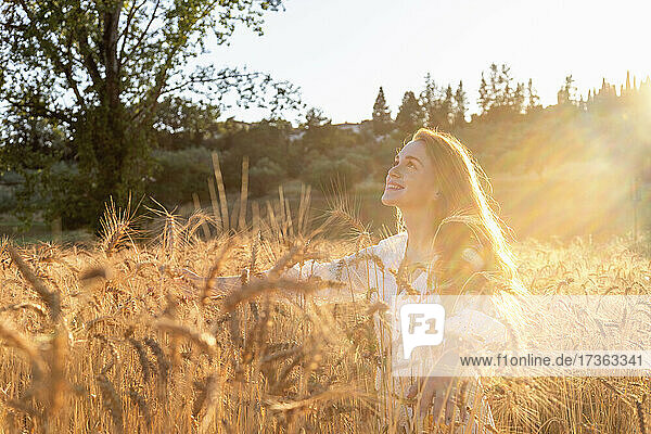 Lächelnde Frau genießt den sonnigen Tag inmitten von Weizenpflanzen auf einem Feld