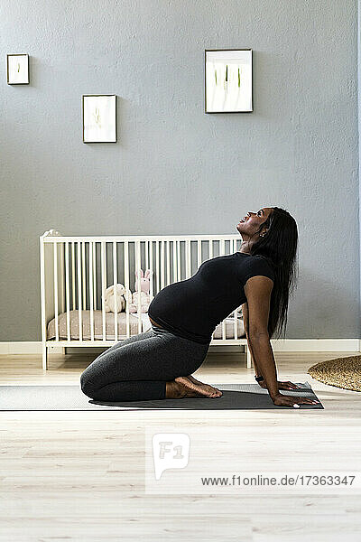 Junge schwangere Frau lehnt sich zurück  während sie im Schlafzimmer Yoga übt