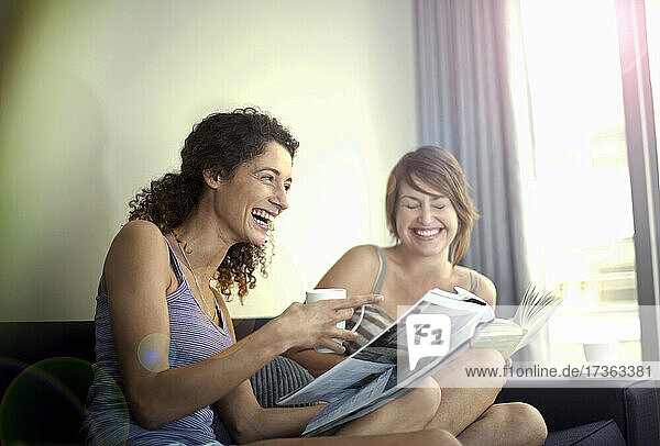 Fröhliche Freundinnen sitzen mit Zeitschriften im heimischen Wohnzimmer