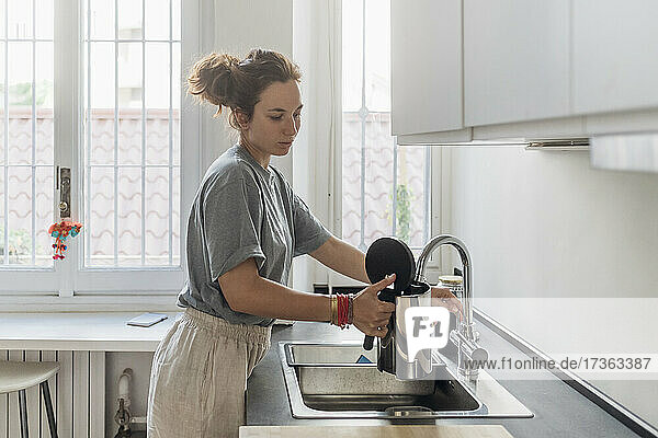 Frau füllt Kaffeekanne aus Wasserhahn in Küche