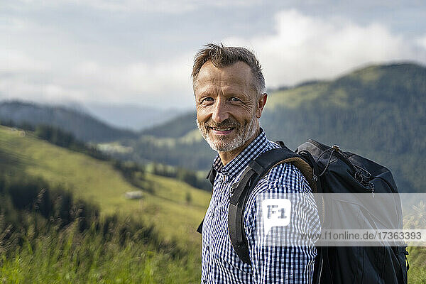 Lächelnder männlicher Wanderer mit Rucksack auf einem Berg