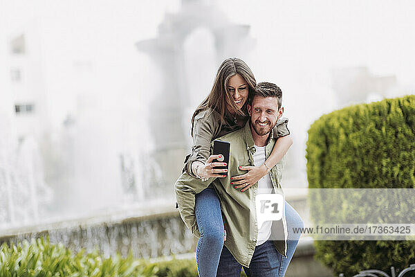 Woman taking selfie through mobile phone while piggybacking on boyfriend