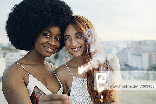 Smiling young lesbian couple holding sparklers during sunset