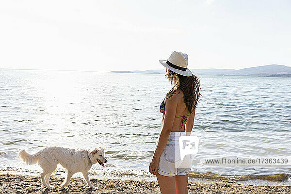 Frau mit Hut schaut auf den Lago Trasimeno und steht neben einem Hund