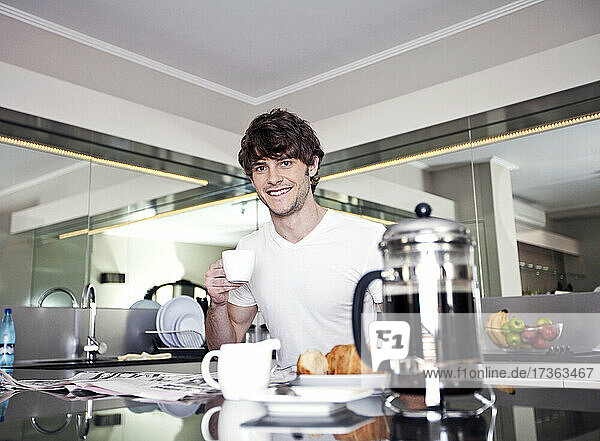 Lächelnder junger Mann beim Kaffee in der Küche