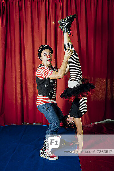 Schockierter männlicher Akrobat hilft einer weiblichen Darstellerin beim Handstand auf der Bühne