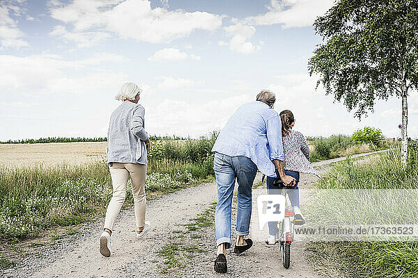 Enkelin fährt Fahrrad  während die Großeltern auf einem unbefestigten Weg laufen