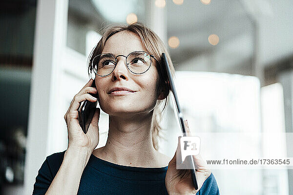 Female professional looking away while talking on smart phone and digital tablet