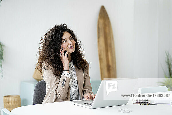 Geschäftsfrau mit Laptop am Schreibtisch  die mit einem Mobiltelefon im Büro spricht
