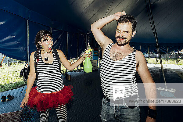 Female performer spraying water on smiling male artist at backstage