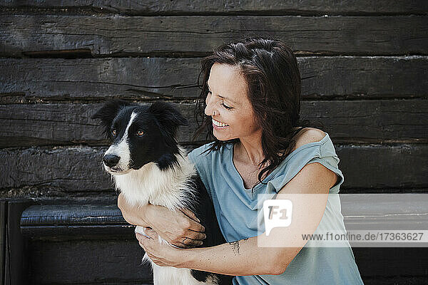 Happy woman hugging Border Collie while sitting in front of cottage