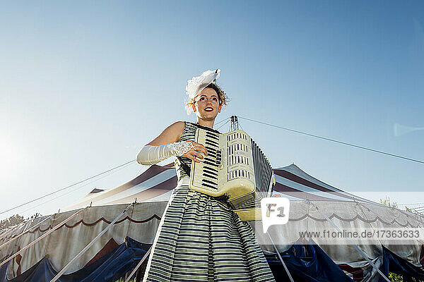 Weibliche Darstellerin spielt Akkordeon vor einem Zirkuszelt