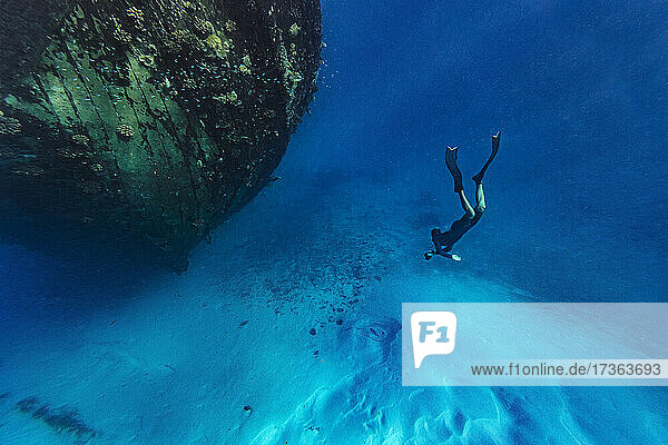 Young man swimming towards abandoned ship undersea