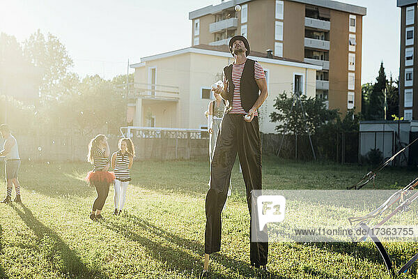 Männlicher Artist jongliert mit Bällen  während er auf Stelzen im Gras steht