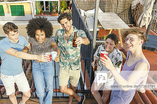 Fröhliche multiethnische männliche und weibliche Freunde stoßen während einer Party auf dem Dach mit Getränken an