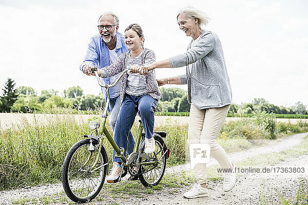 Älterer Mann und Frau  die einem Mädchen beim Fahrradfahren auf einem Feldweg helfen