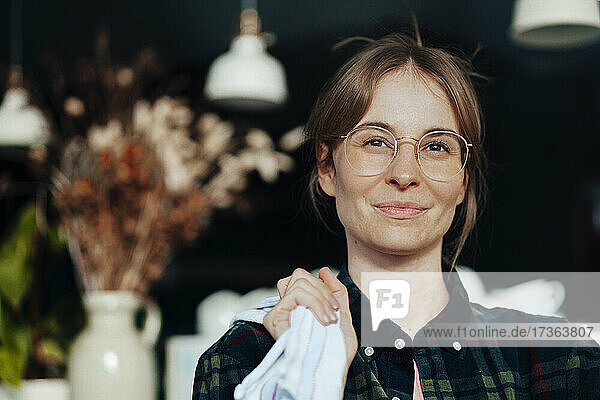 Junge Kaffeehausbesitzerin mit Brille hält Lappen