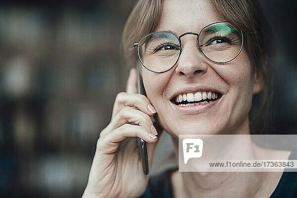 Happy young businesswoman wearing eyeglasses talking on smart phone
