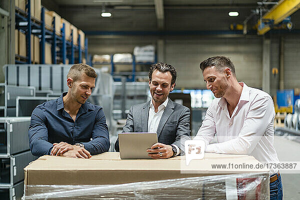 Smiling male professionals discussing over digital tablet at industry
