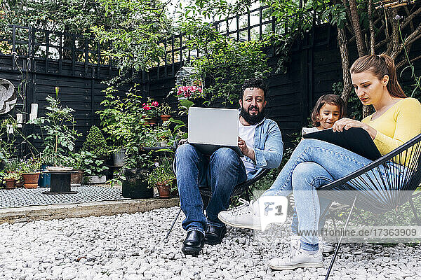 Mann mit Laptop sitzt bei einer Frau  die ein Mädchen im Hinterhof unterrichtet