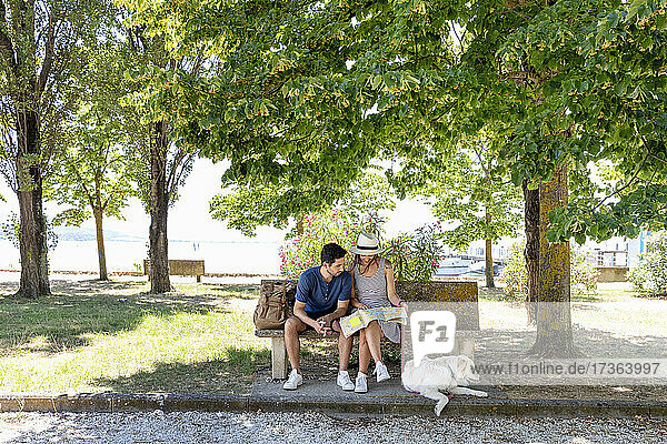 Touristisches Paar  das auf einer Bank sitzend die Karte überprüft