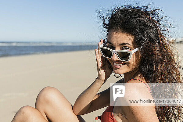 Lächelnde junge Frau mit Sonnenbrille  die am Strand sitzt