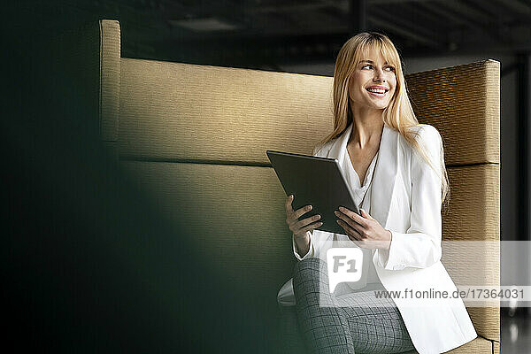 Smiling businesswoman looking away while sitting with digital tablet on seat