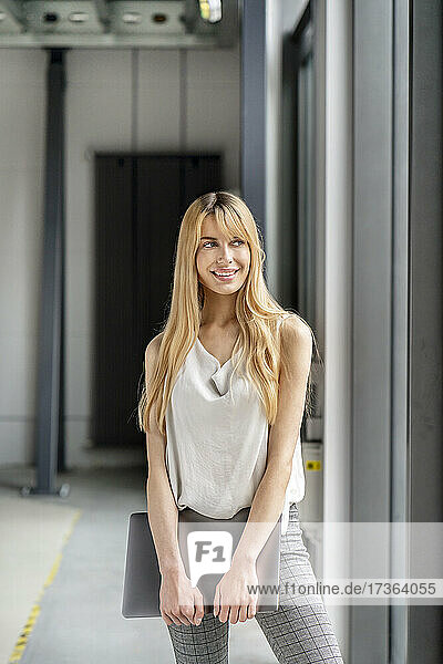 Young blond businesswoman holding laptop at workplace