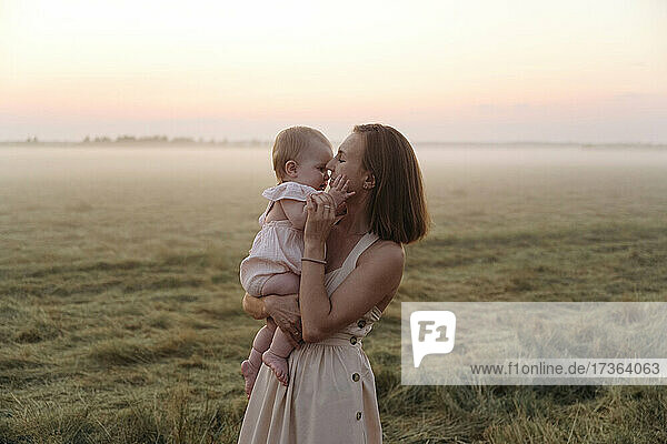 Mutter trägt niedliche Tochter auf einem Feld bei Sonnenuntergang