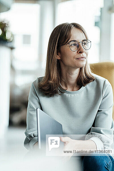 Weibliche Fachkraft schaut weg  während sie mit einem digitalen Tablet in einem Café sitzt