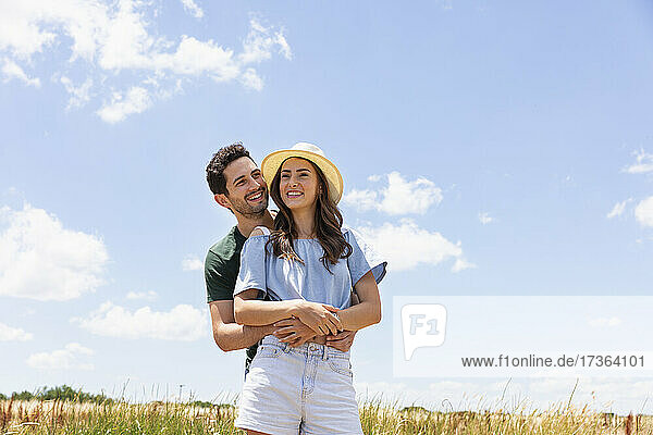 Smiling boyfriend standing behind girlfriend on sunny day