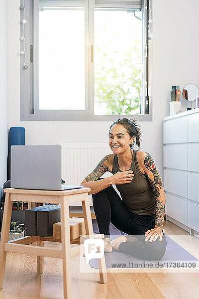 Lächelnde Frau  die einen Laptop benutzt  während sie zu Hause Yoga macht