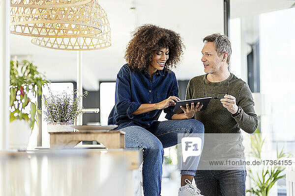 Mature male professional looking at businesswoman using digital tablet while discussing in office