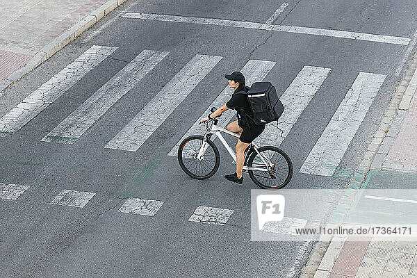 Female delivery person with backpack riding bicycle at crossroad
