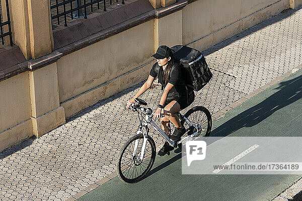 Weibliche Lieferperson fährt Fahrrad auf der Straße an einem sonnigen Tag