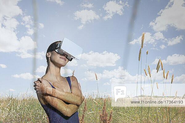 Young woman with virtual reality simulator hugging self on field