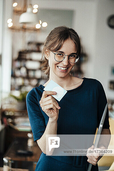 Happy businesswoman holding laptop showing card in cafe