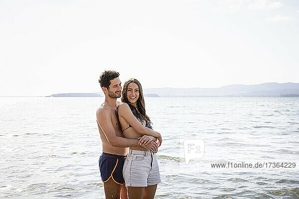 Lächelnder Freund  der seine Freundin von hinten umarmt  während er im See steht