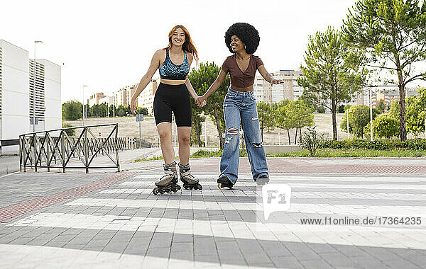 Young female friends holding hands while skating in city