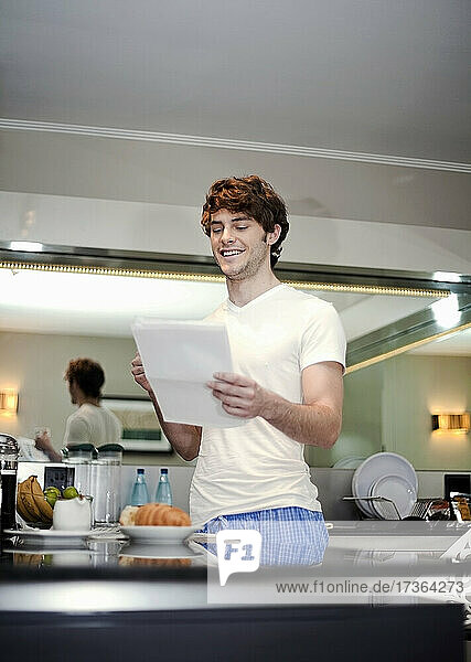 Lächelnder junger Mann  der in der Küche stehend einen Brief liest