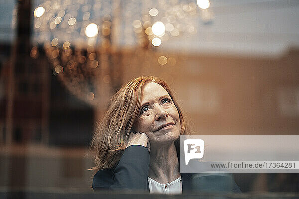 Nachdenkliche Frau mit blondem Haar durch ein Glasfenster gesehen