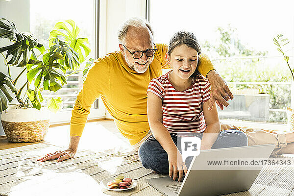 Enkelin benutzt Laptop  während sie mit Großvater zu Hause sitzt