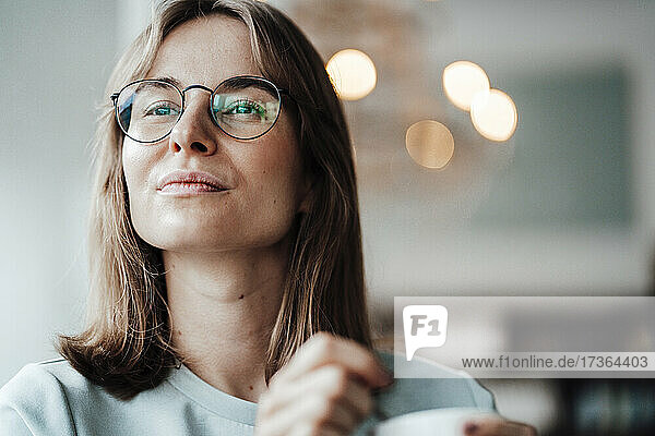 Nachdenkliche junge Frau mit braunem Haar und Brille schaut weg