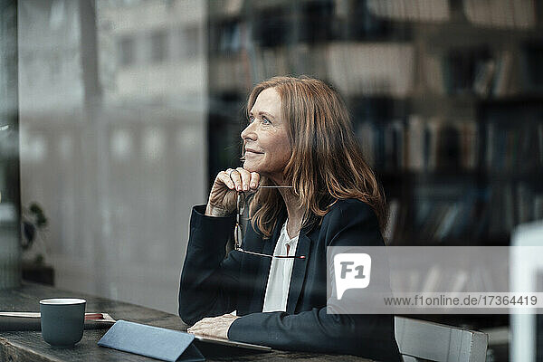 Thoughtful senior businesswoman sitting with hand on chin in cafe