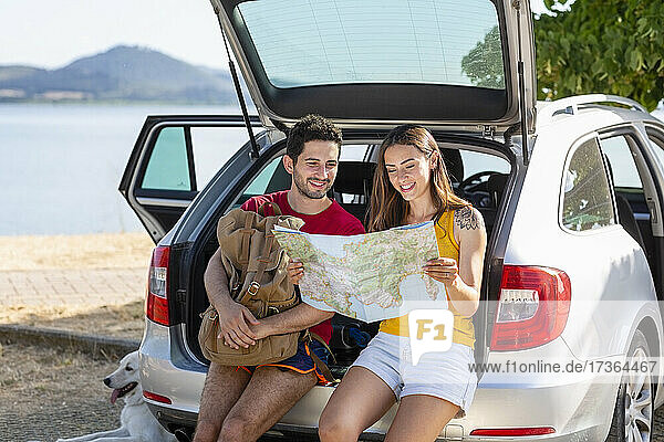 Lächelndes Paar  das im Kofferraum des Autos sitzend die Karte überprüft